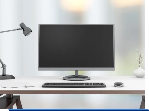 Ein Schreibtisch auf dem ein Computer Monitor, eine Tastatur, eine Maus und eine Schreibtischlampe zu sehen sind.